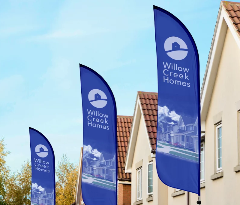 A feather style flag presenting the Willow Creek Homes brand in front of a new-build house estate.