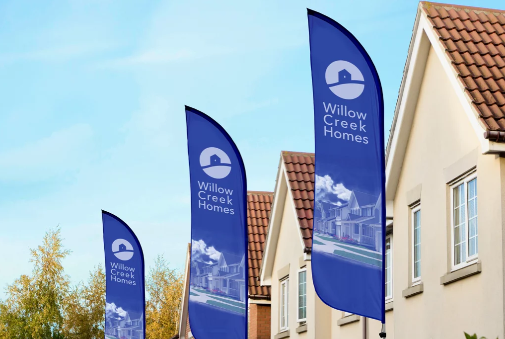 A feather style flag presenting the Willow Creek Homes brand in front of a new-build house estate.