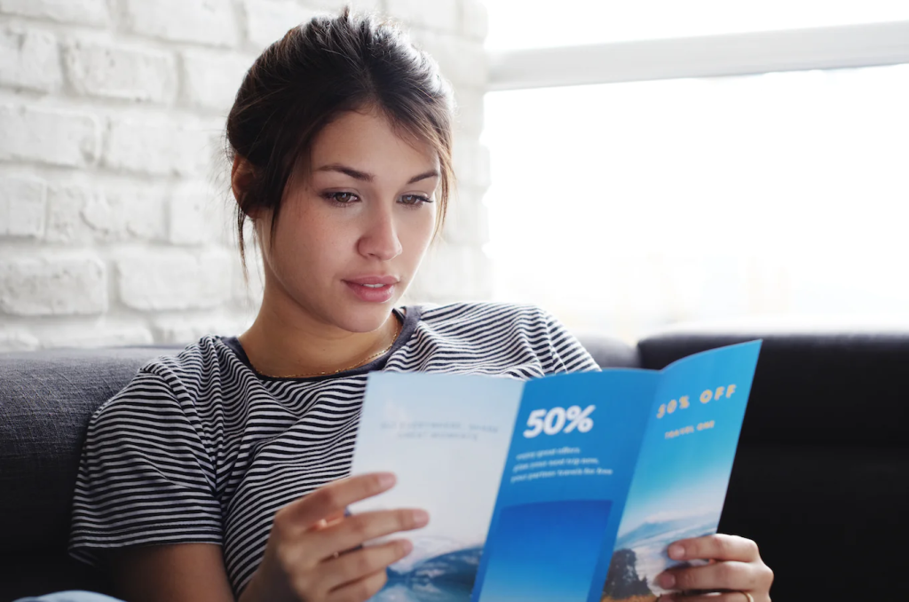 A woman in a striped t-shirt sitting on a sofa reading a blue 50% off advertising leaflet.