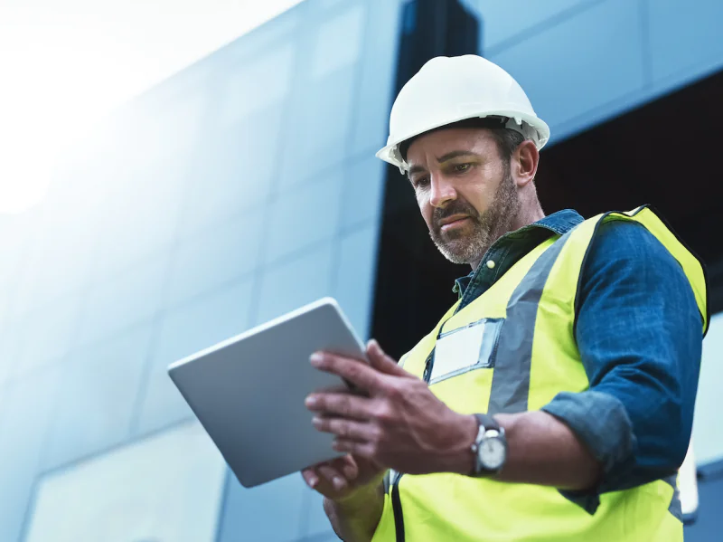 A man in PPE looking at a tablet on a building site.