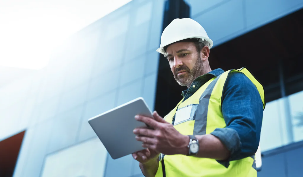 A man in PPE looking at a tablet on a building site.