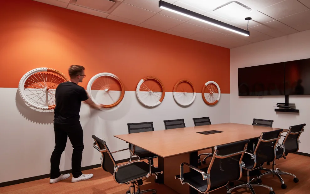 A man installing a wall feature on an orange and white horizontally split wall. The feature is 5 bike wheels painted orange and white.